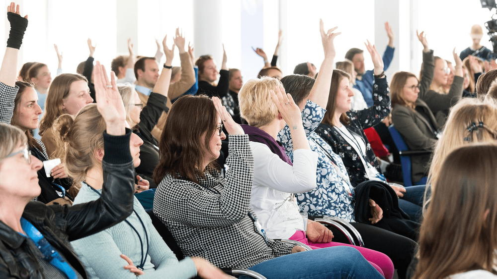 Dein Beitrag ist gefragt! Bild mit Personen im Publikum die sich melden